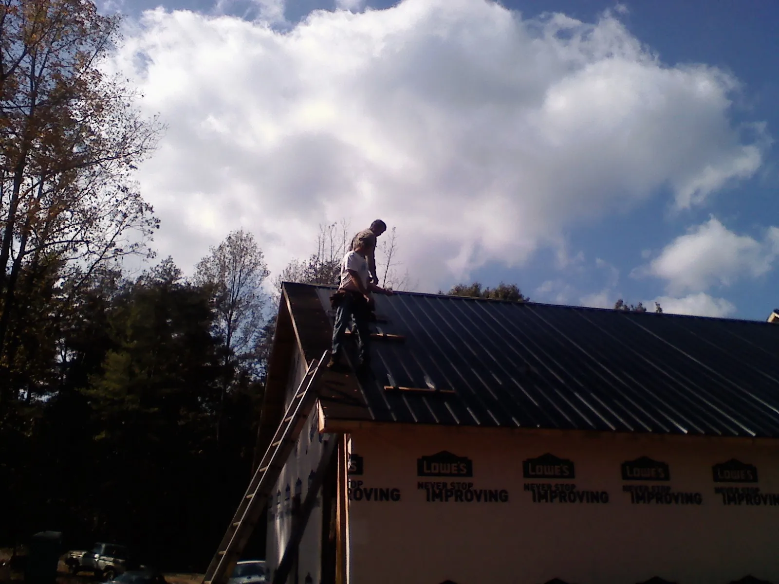 Roofer fastening dark metal panels high against a cloudy sky, from a Roof Inspection job in Freeport